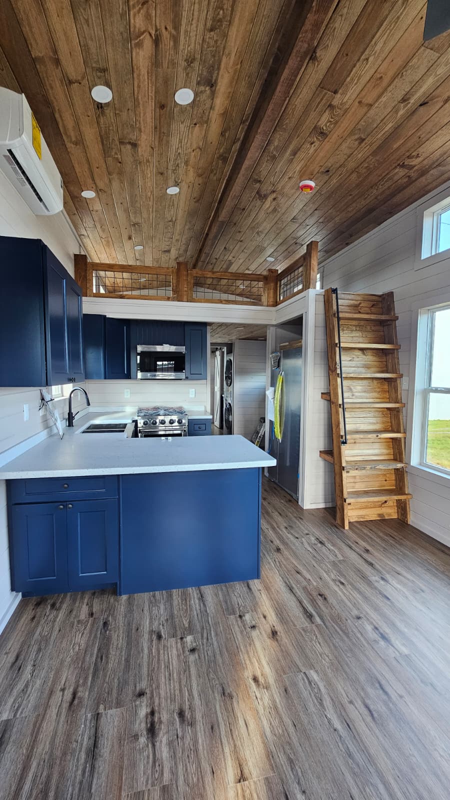 Park model home kitchen with navy island, quartz counters, loft ladder and wood ceiling